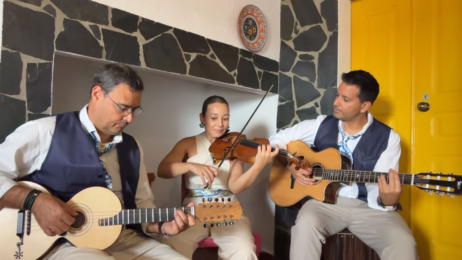 O trio a tocar dentro de casa, junto a uma parede de pedra