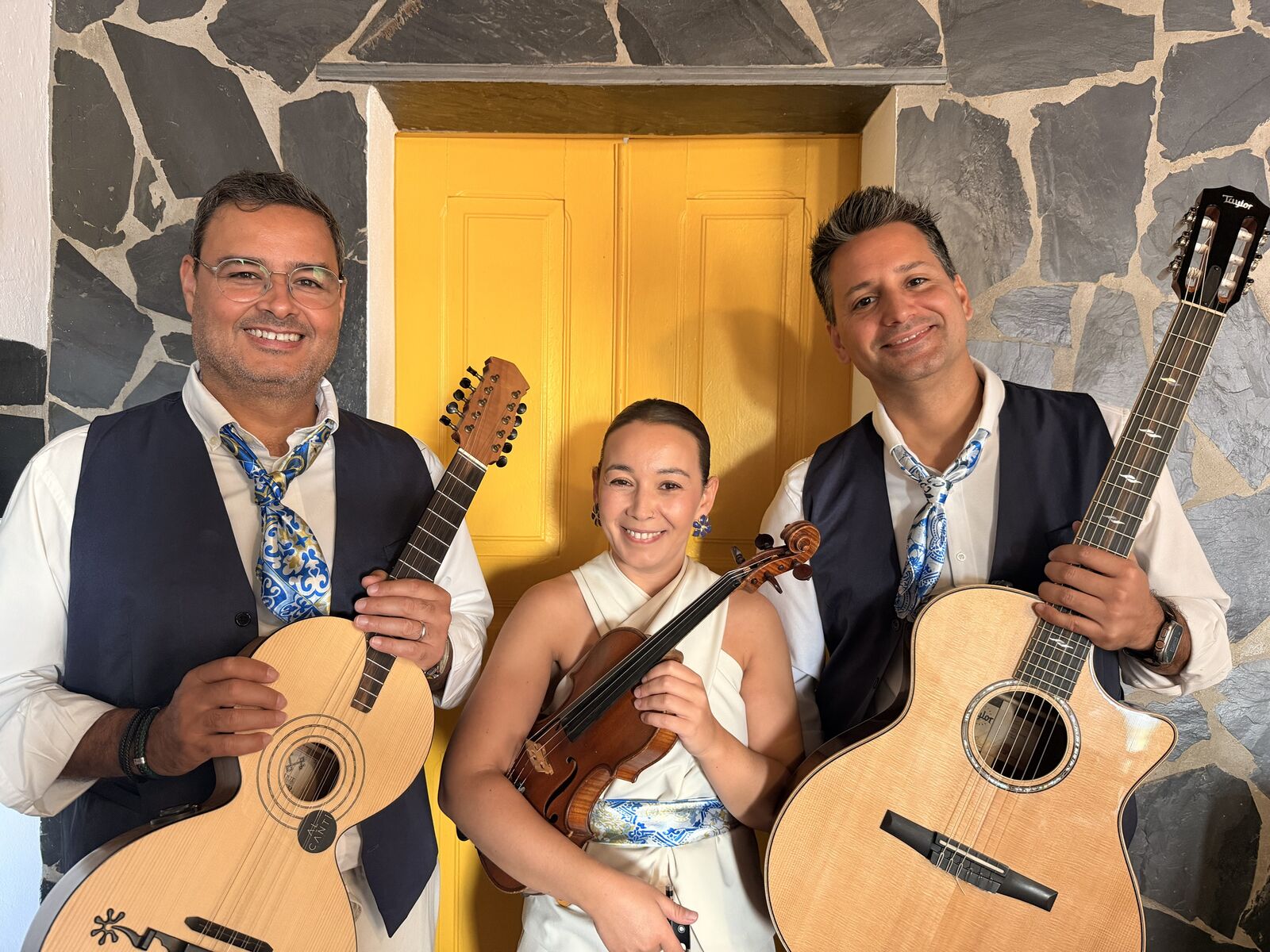 Os três músicos sorridentes em frente à porta amarela