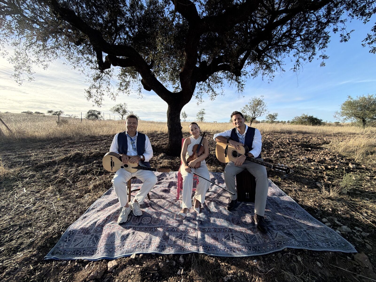 O trio sentado debaixo de um sobreiro, com o campo ao fundo
